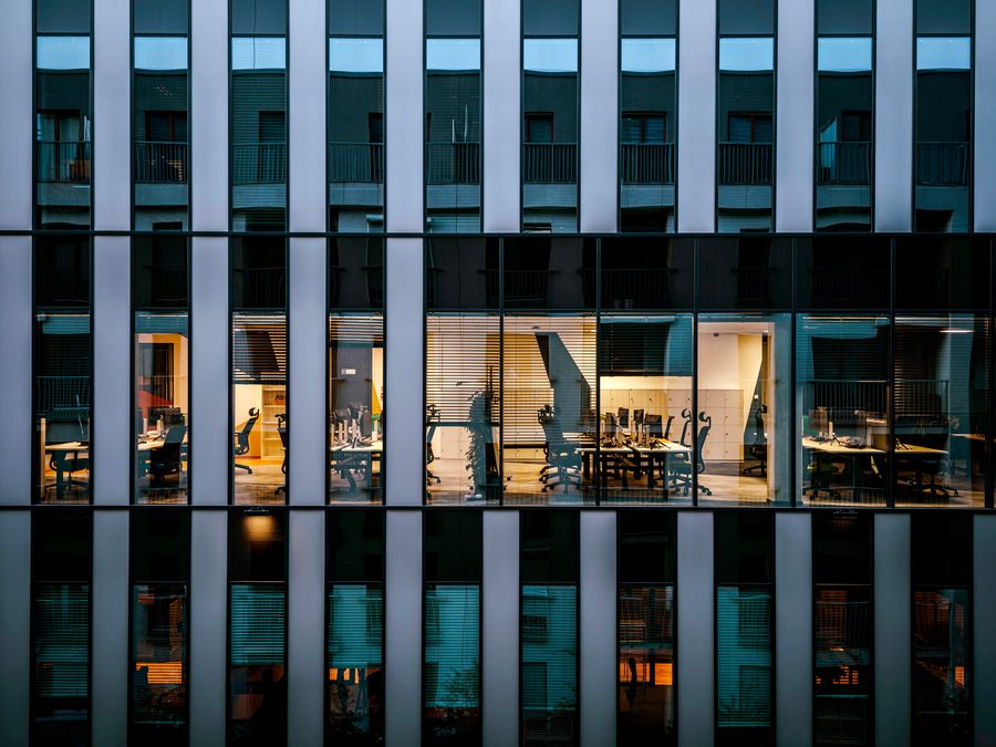 A modern commercial building at dusk with lit offices behind a patterned facade.