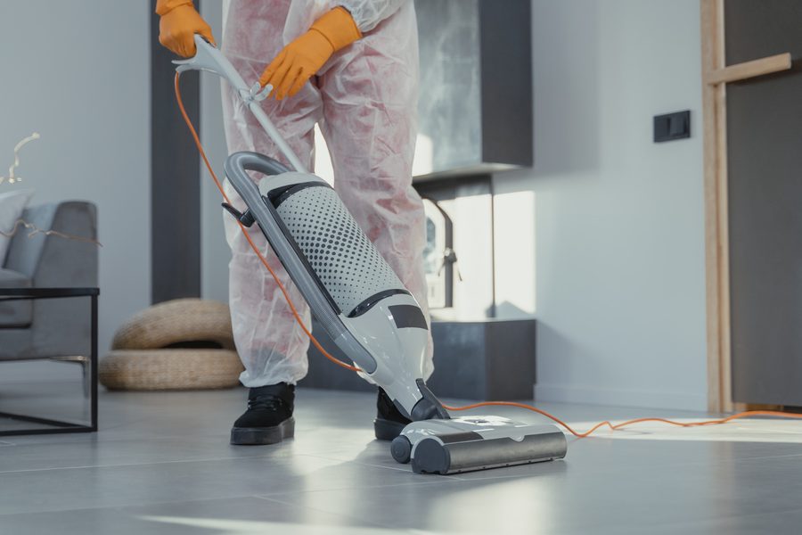 A technician in protective coveralls running a floor machine across a hard surface floor.