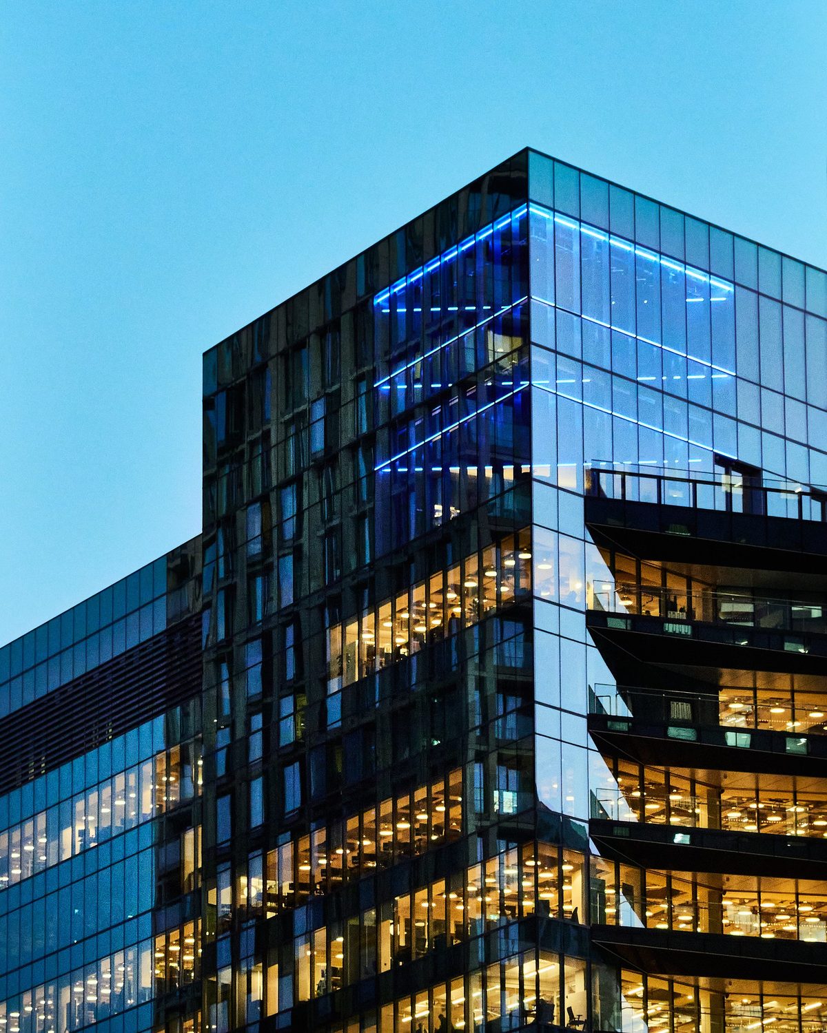 A modern glass office tower at dusk with warmly lit floors, the kind of commercial property P23 Management maintains.
