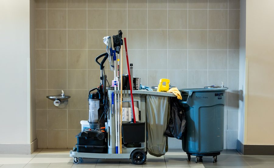 A stocked janitorial cart and waste bin staged in a tiled corridor.