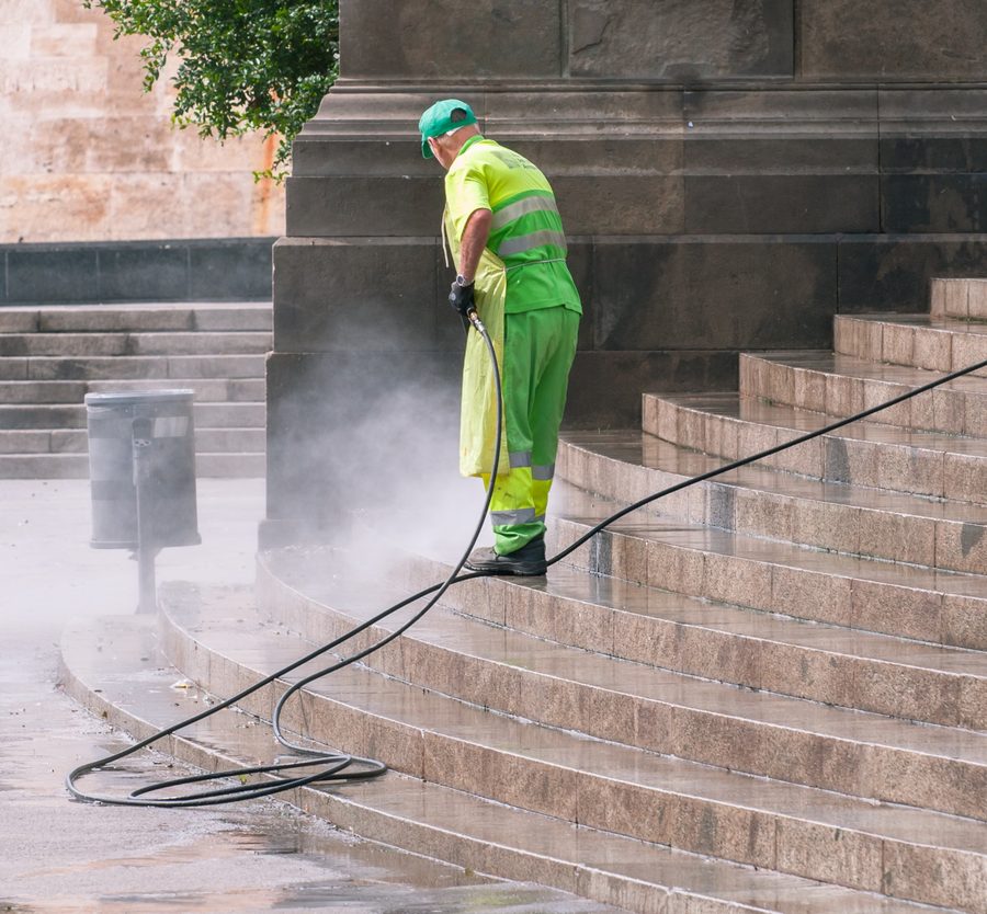 A worker in high-visibility gear pressure washing wide stone steps.