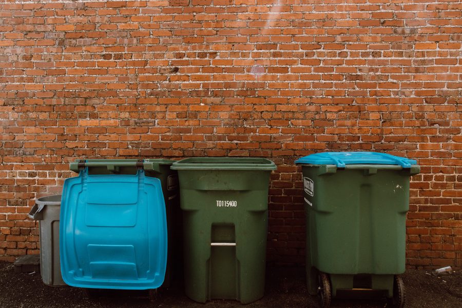 Three wheeled waste and recycling bins lined up against a brick wall.